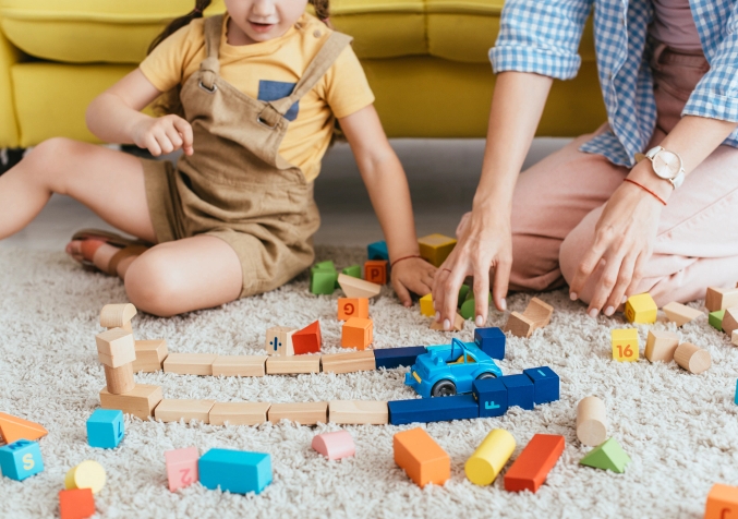 Mother and Young Girl Playing with Woooden Blocks on Carpet